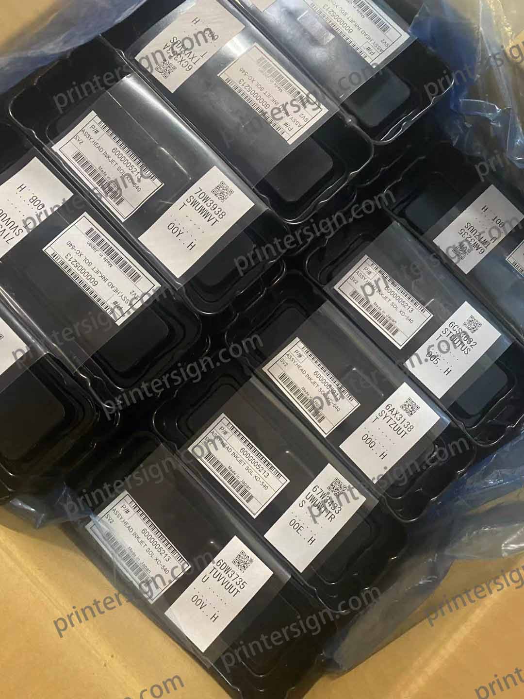 A close-up view of multiple black plastic containers stacked together, each labeled with barcodes and product information.