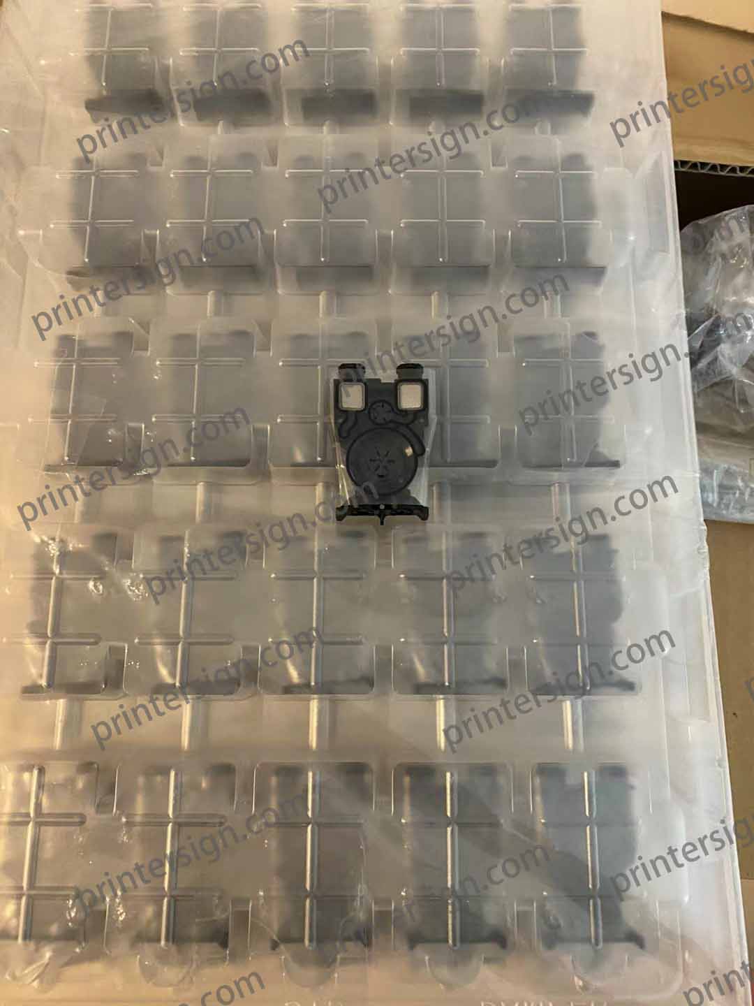 A close-up view of a plastic organizer tray containing small gray components, with one black component positioned in the center. The tray features multiple compartments for holding the items securely.