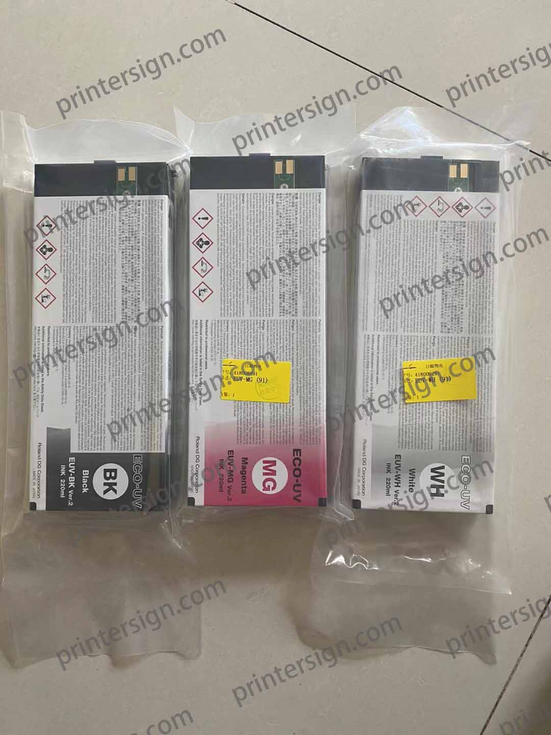 Three packaged ink cartridges labeled Black, Magenta, and White, with safety information printed on the packaging, displayed on a light-colored surface.
